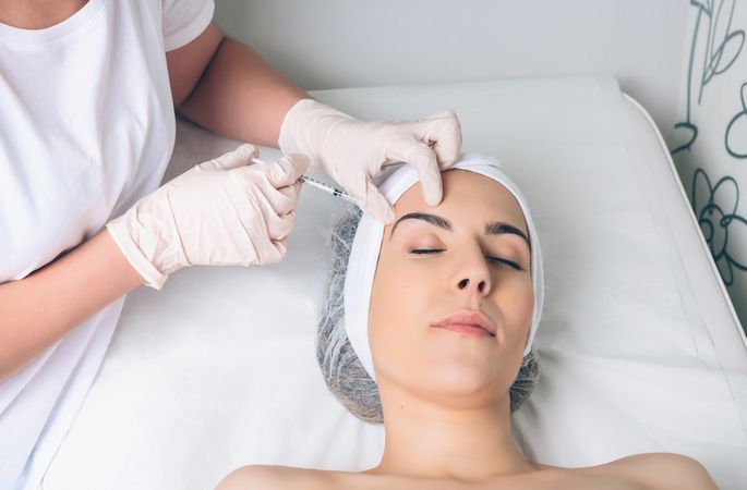 Aesthetician's hands injecting botox into woman's forehead in a beauty salon