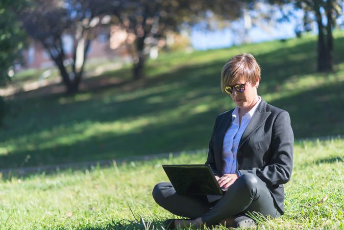 Woman sitting cross legged in park with laptop