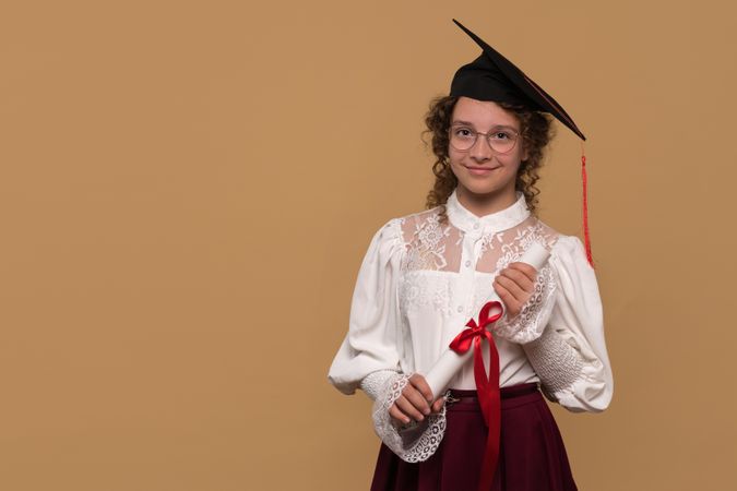 Teen girl in graduation cap holding diploma with red ribbon.
