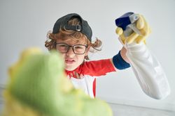 Curly boy in superhero clothes cleaning camera in studio