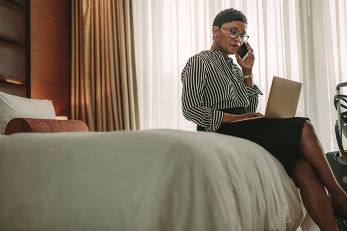 Businesswoman on tour working with laptop computer and mobile phone in hotel room