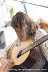 Female with hair hiding her face in wool sweater strumming acoustic guitar 0KjKMb