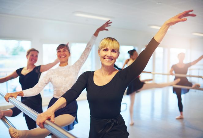 Group of smiling women stretching at barre in dance studio