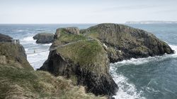 Tourist walking on rope bridge suspended between cliffs in Northern Ireland