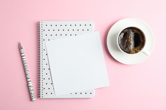 Cup of coffee with copybook and pen on color background, top view
