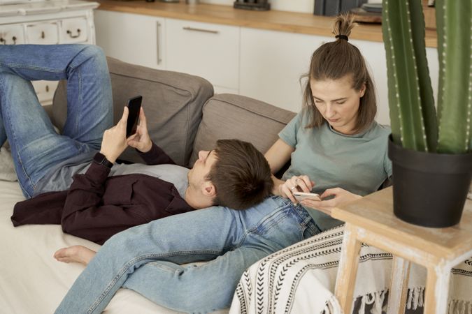 Chilling couple spending time together on sofa browsing smartphone