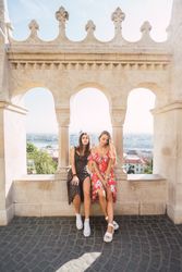 Stylish girl friends on old ornamental wall of building