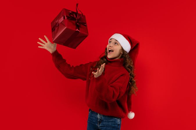 Excited girl in Santa hat tosses red Christmas gift.