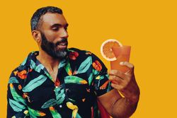 Black male sitting down and looking at his cocktail in yellow room, copy space