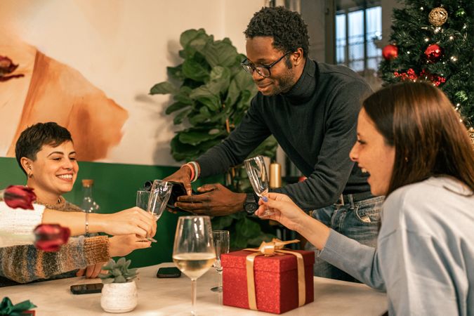 Happy diverse friends sharing and pouring champagne at a festive Christmas party.