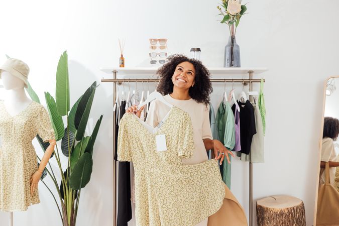 Happy Black woman with floral print dress in bright clothes shop