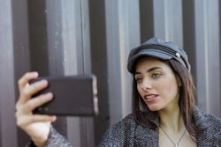 Charming Hispanic lady taking selfie near wall