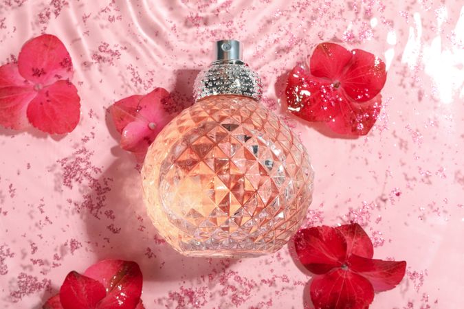 Glass perfume bottle in water with pink background and flowers