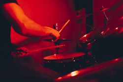 Anonymous man with drumsticks playing on drums in redness