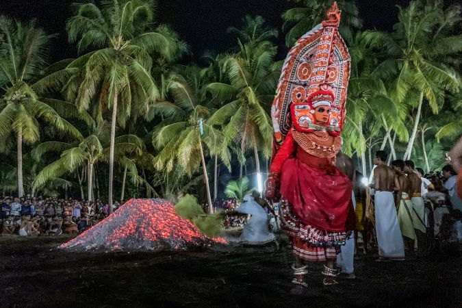 Man performing Theyyam ritual form of dance worship with men at night