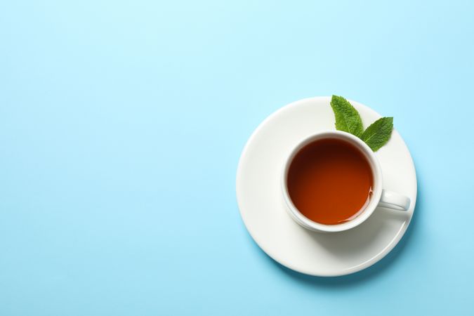 Cup of tea and mint leaves on blue background, copy space