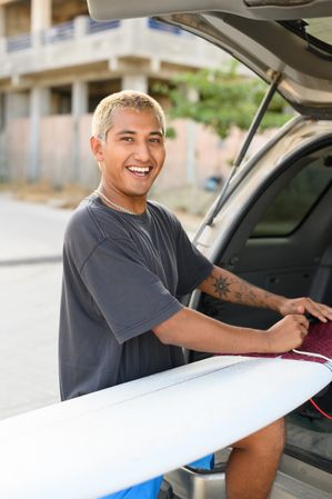 Happy man with surfboard in car on street