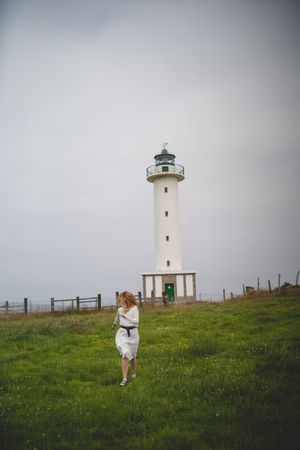 Woman running in green meadow near lighthouse