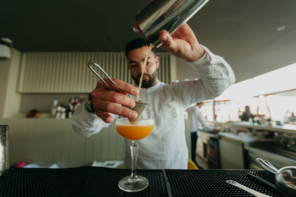 Barman pouring cocktail and alcoholic drinks from shaker in a bar.