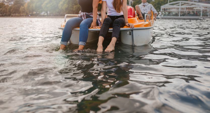 Cropped shot of young women sitting pedal boat front with feet in water