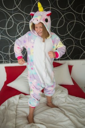 Cheerful girl in unicorn pajama having fun on bed