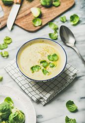 Brussels sprout soup, garnished with fresh sprouts, next to wooden board, vertical composition