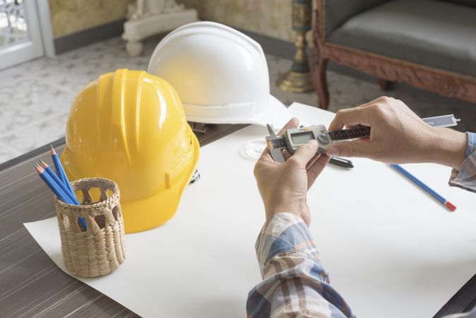 Person at work desk with hard hat, pencils, magnifying glass and calipers