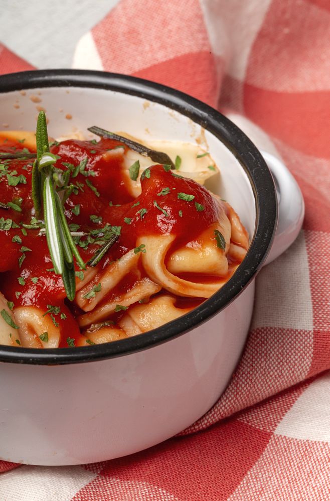 Bowl of delicious ravioli with tomato sauce and rosemary on table cloth