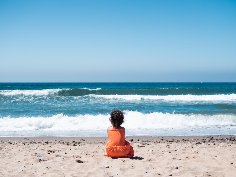 Little girl sitting on beach and admiring view
