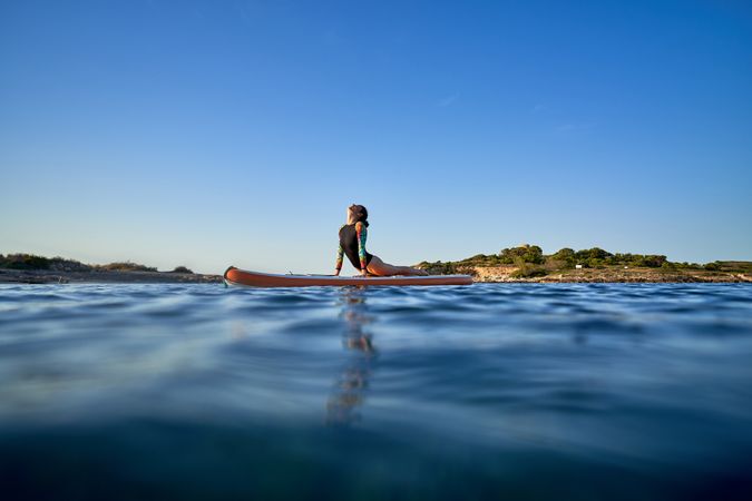 Fit sportswoman taking Cobra pose on SUP board in sea