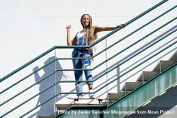 Happy female in denim overalls standing on skateboard on stairs 421L35
