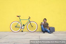 Man sitting in front of yellow wall with bike listening to music 5QvWm4
