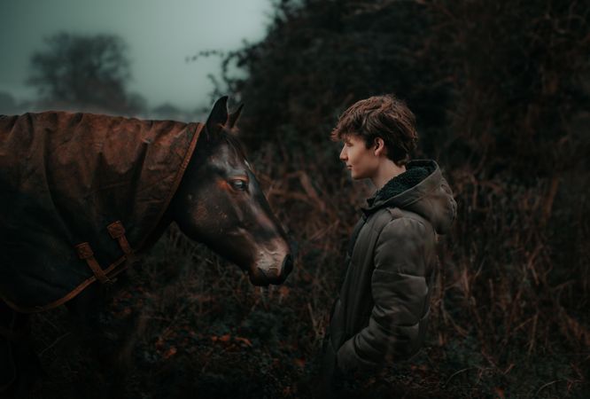 Side view of teenage of boy beside dark horse