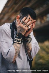 Tattooed young punk goth man burying face in hands with spike bracelets 41lVp5