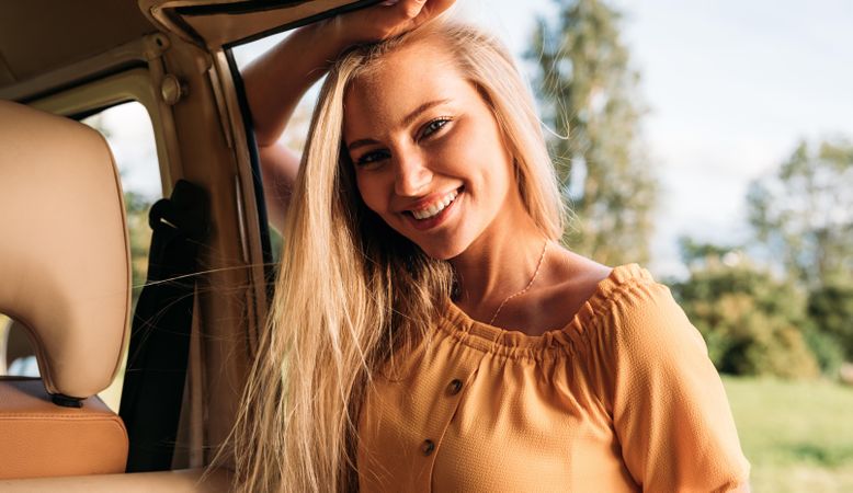 Close up of blonde woman leaning on a van door in a field