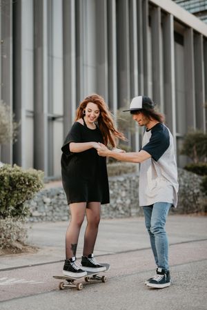 Man helping girlfriend to skate on road
