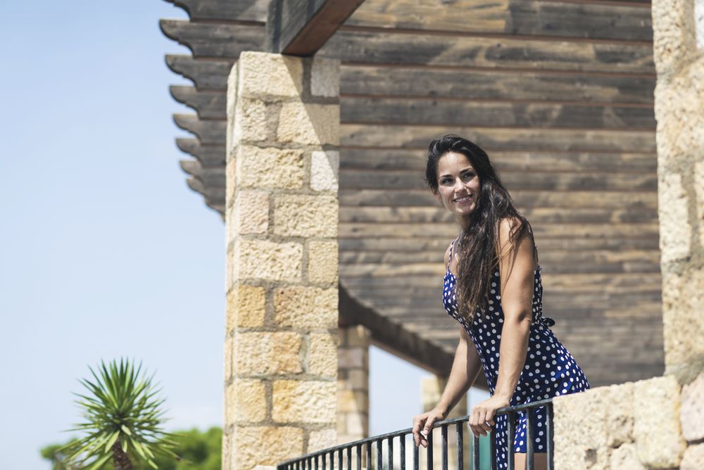 Smiling Latina woman in blue dress leaning on hand rail while looking in distance