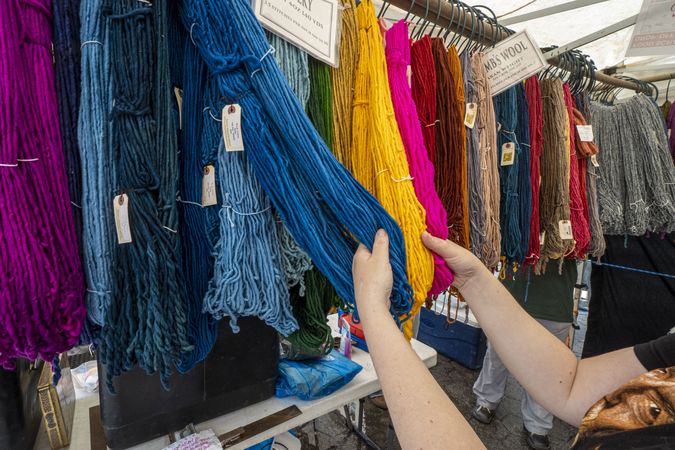 Person’s hands touching brightly colored skeins on Merino wool at a farmers market