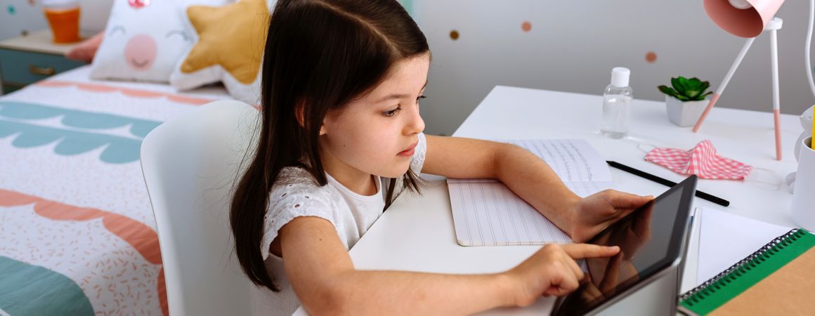 Girl studying at home with tablet and mask on table