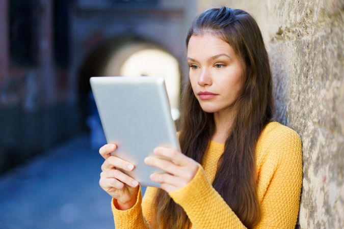 A Young Woman Engaged in Using a Tablet While Outdoors in a Lively Urban Environment