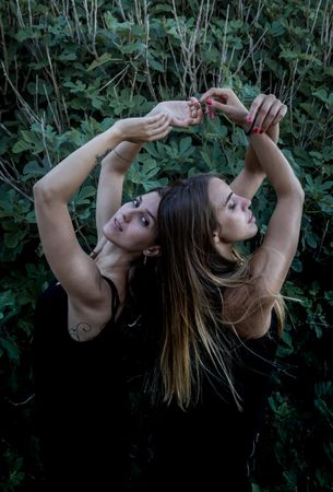 Young women posing near green bush
