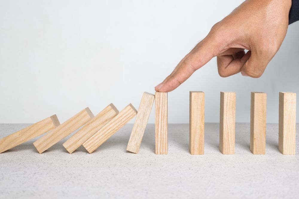 male hand stop falling wooden blocks. domino effect or risk protection strategy concept