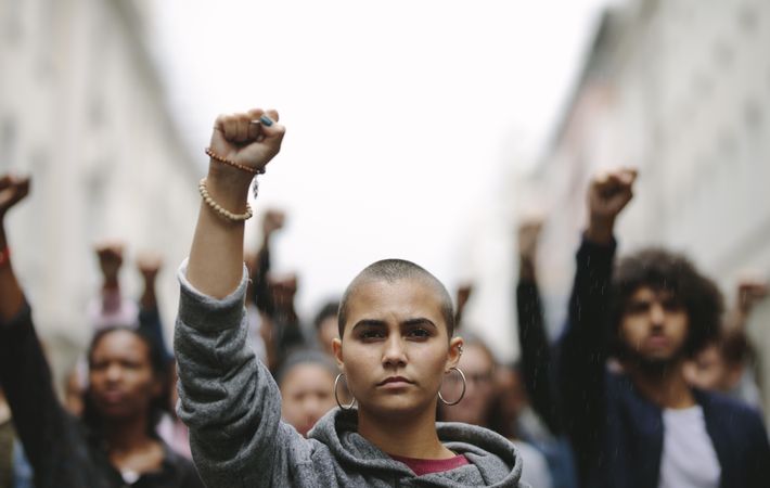 Young woman protesting on the street with her fist raised in air