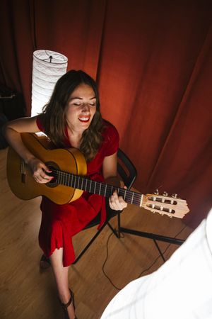 Woman singing and playing guitar on stage in lamplight