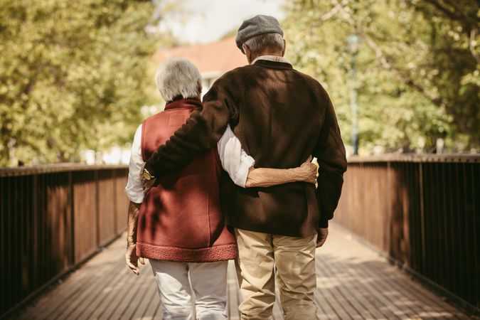 Rear view of older couple walking through a park with their arms around each other in the fall