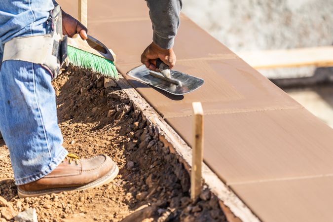 Construction Worker Using Trowel On Wet Cement Forming Coping Around New Pool