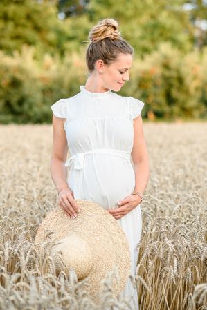 Happy pregnant woman standing in wheat field