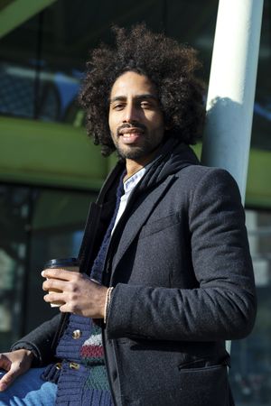 Portrait of smiling handsome Black man in casual wear posing for the camera with take away coffee outdoors