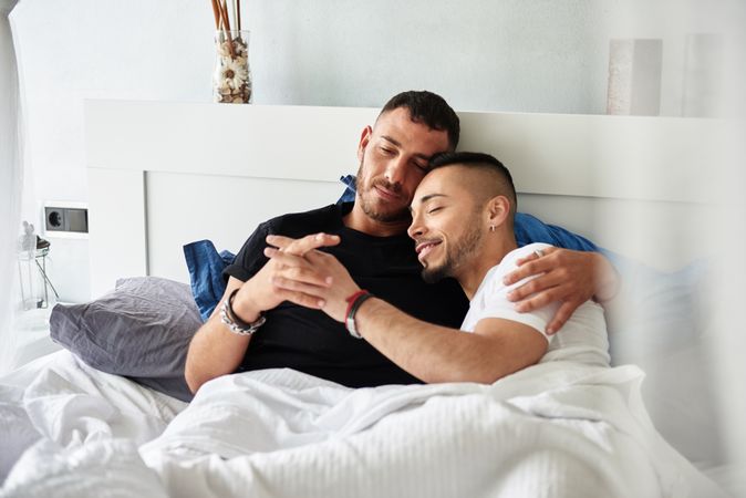 Smiling gay couple hugging on bed