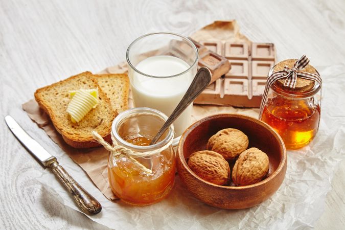 Buttered toast with milk, whole walnuts, chocolate, knife and jam on craft paper